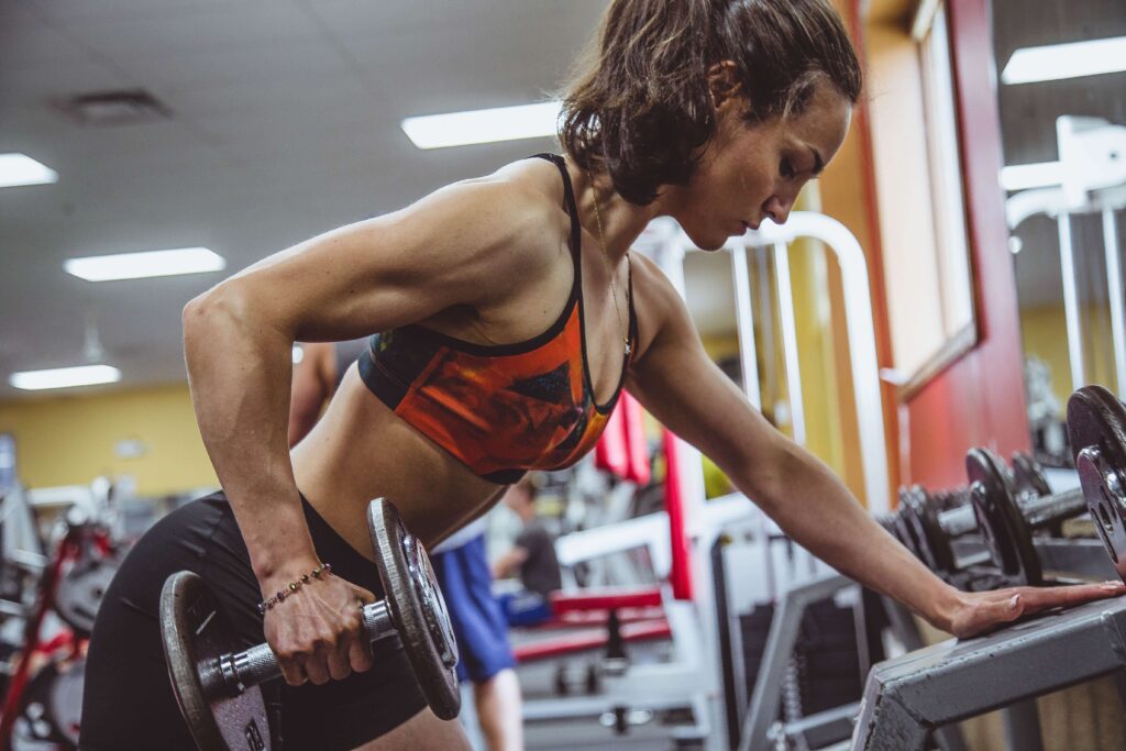 A woman in athletic wear does a bent-over dumbbell row, focused on strength training in a gym.