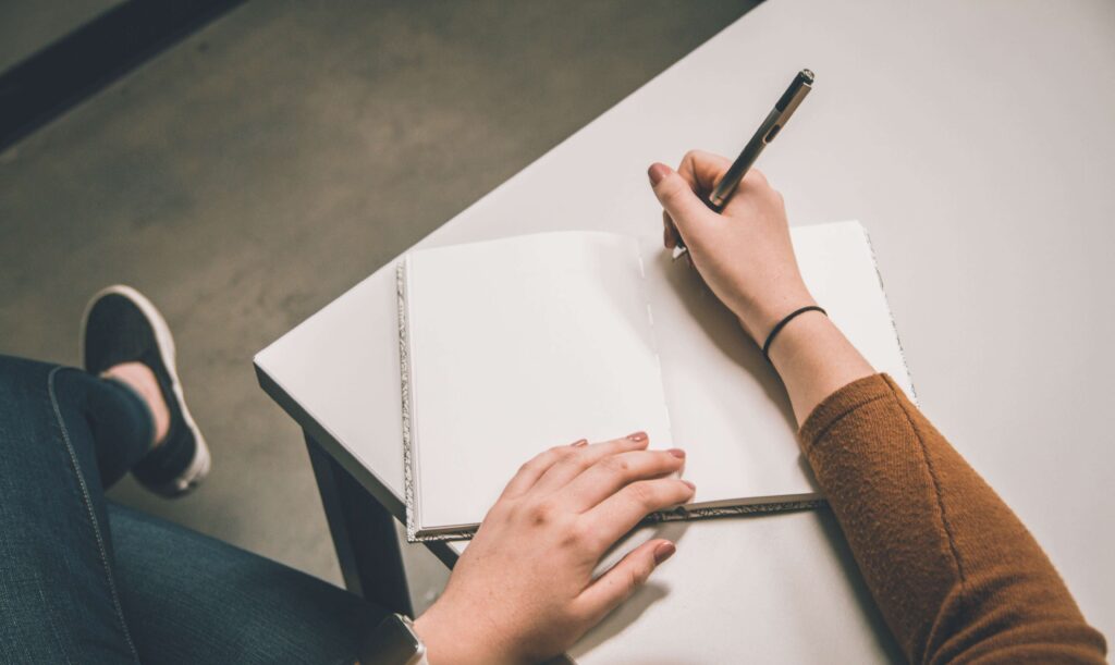 A person in a brown shirt writes in a notebook, reflecting a calm interest in therapies.