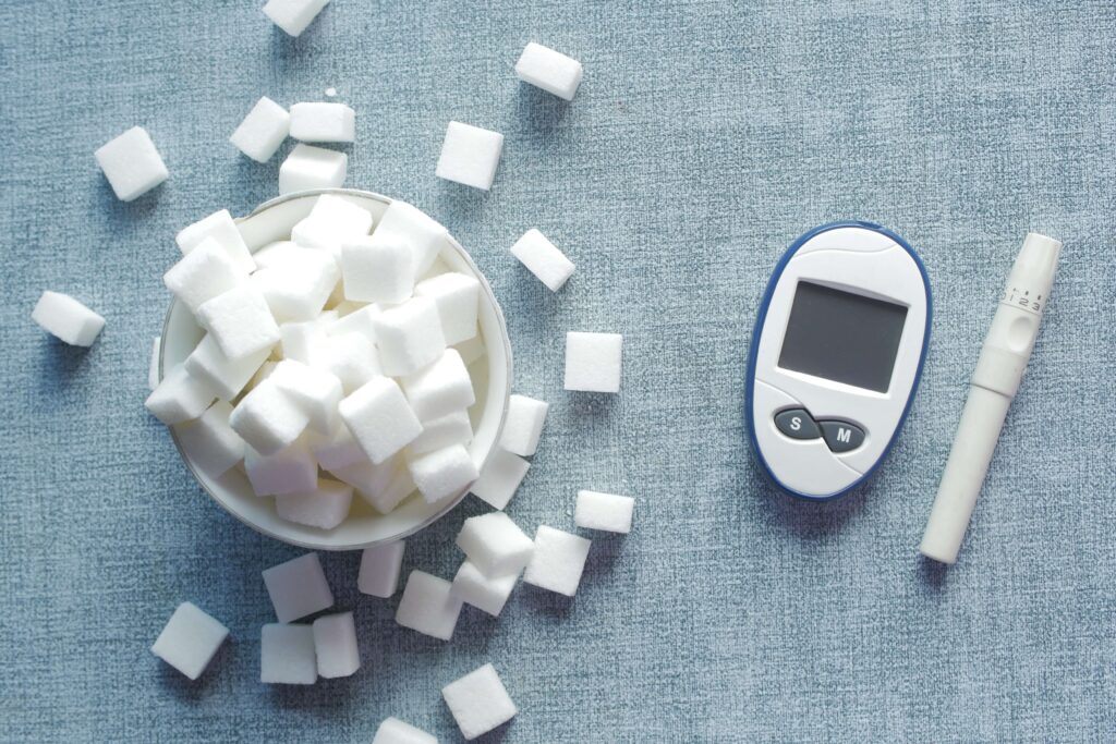 A bowl of sugar cubes with a glucose meter and lancet device, symbolizing blood sugar management.