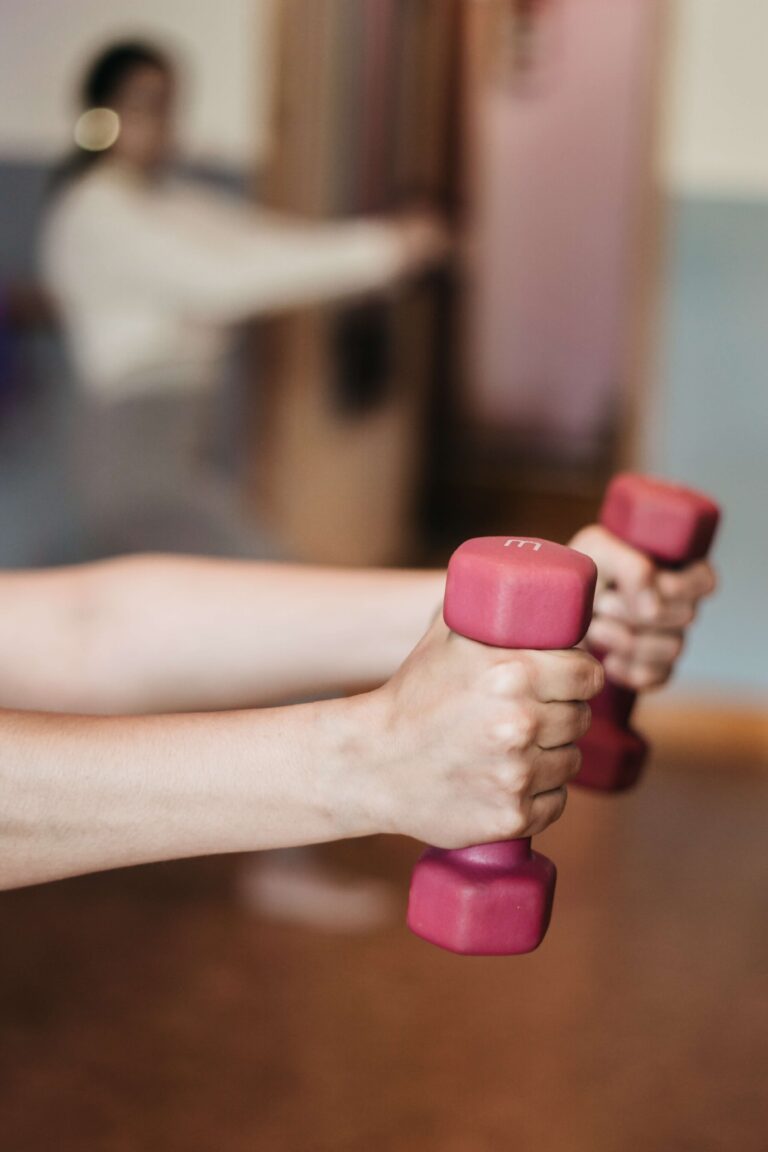 Close-up of hands holding pink dumbbells, extended forward, illustrating strength training.