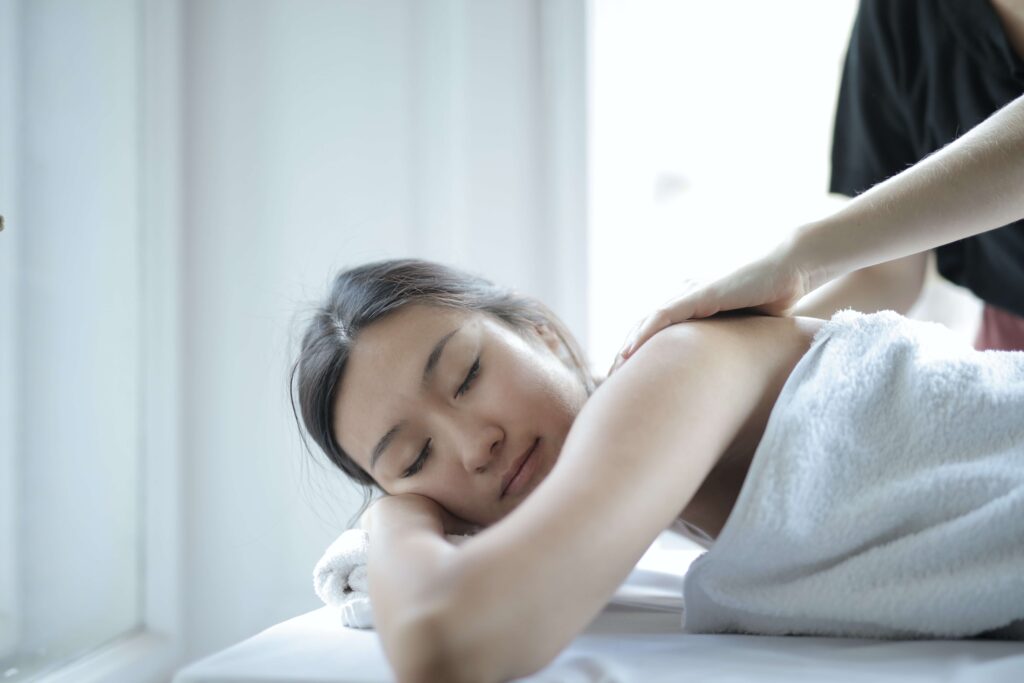 A woman lies on a massage table with her back being gently massaged in a bright room. Massage.