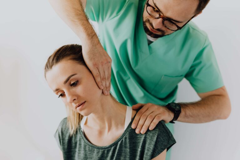A woman sits as a man in green scrubs adjusts her neck in a bright, clinical setting. Chiropractor.