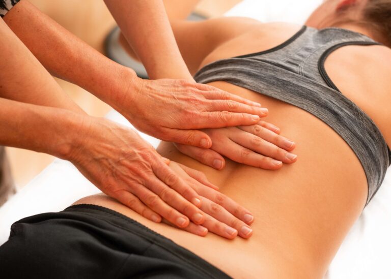 A person in a gray sports bra receives a back massage with pressure applied to their lower back.