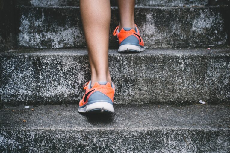 A person in orange and gray athletic shoes walking up concrete steps. Patient care.
